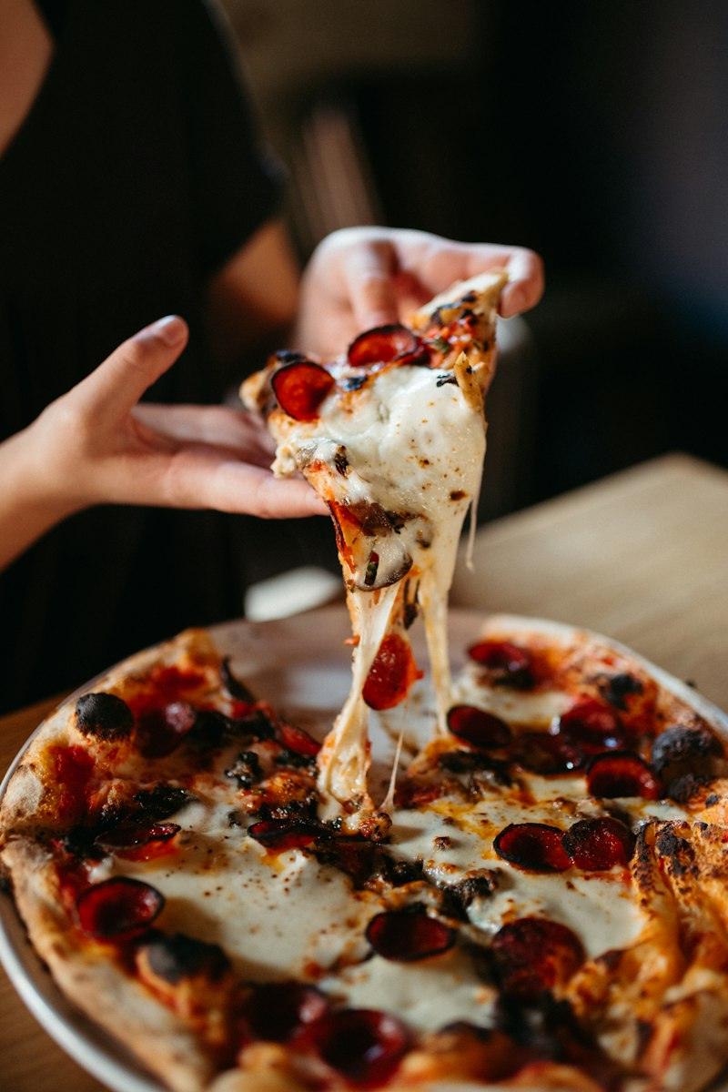 Un trancio di pizza sollevato, con la mozzarella che fila